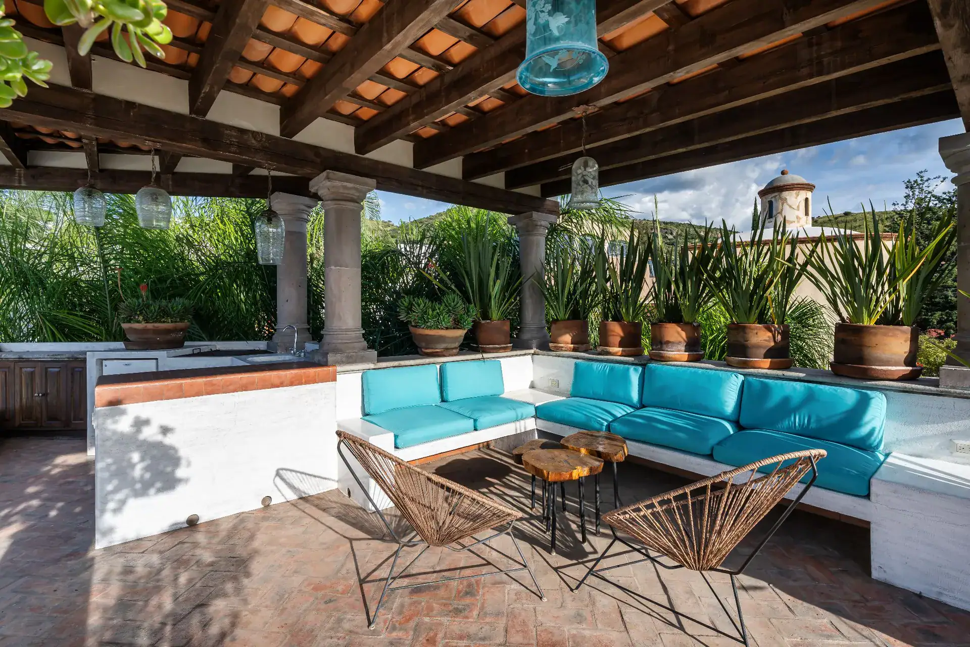 Casa Dos Casas, rooftop terrace with a turquoise cushioned built-in sofa, wire chairs and a tiled pergola, San Miguel de Allende