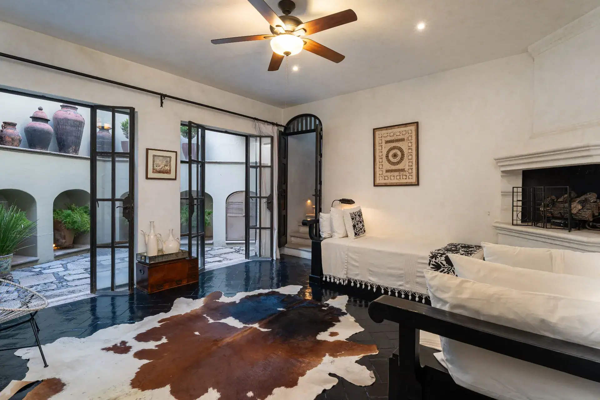 Casa Dos Casas, bedroom with a cowhide rug, white daybed, fireplace and glass doors to a courtyard, San Miguel de Allende