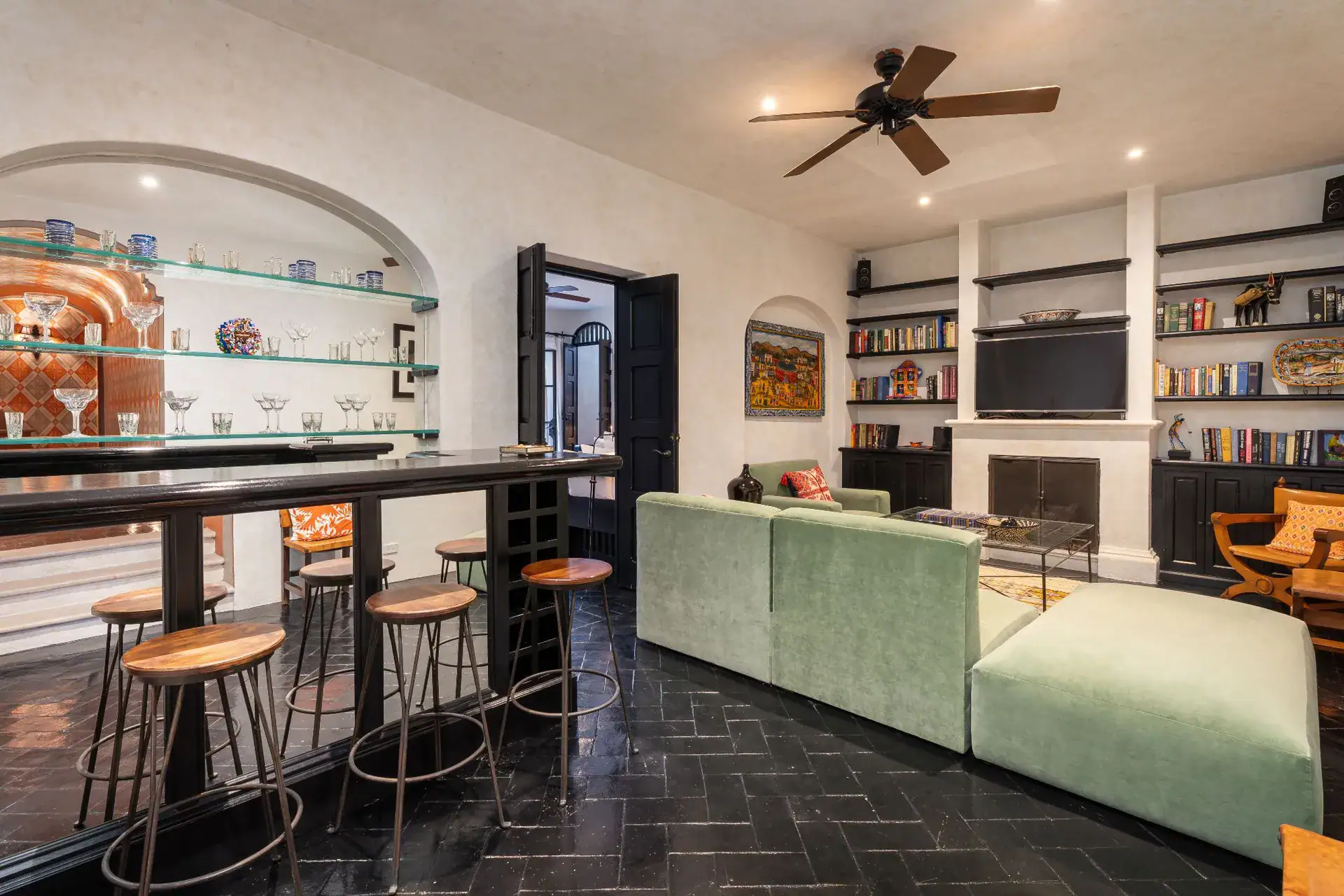 Casa Dos Casas, family room with a bar and stools beside green sectional seating and a fireplace, San Miguel de Allende