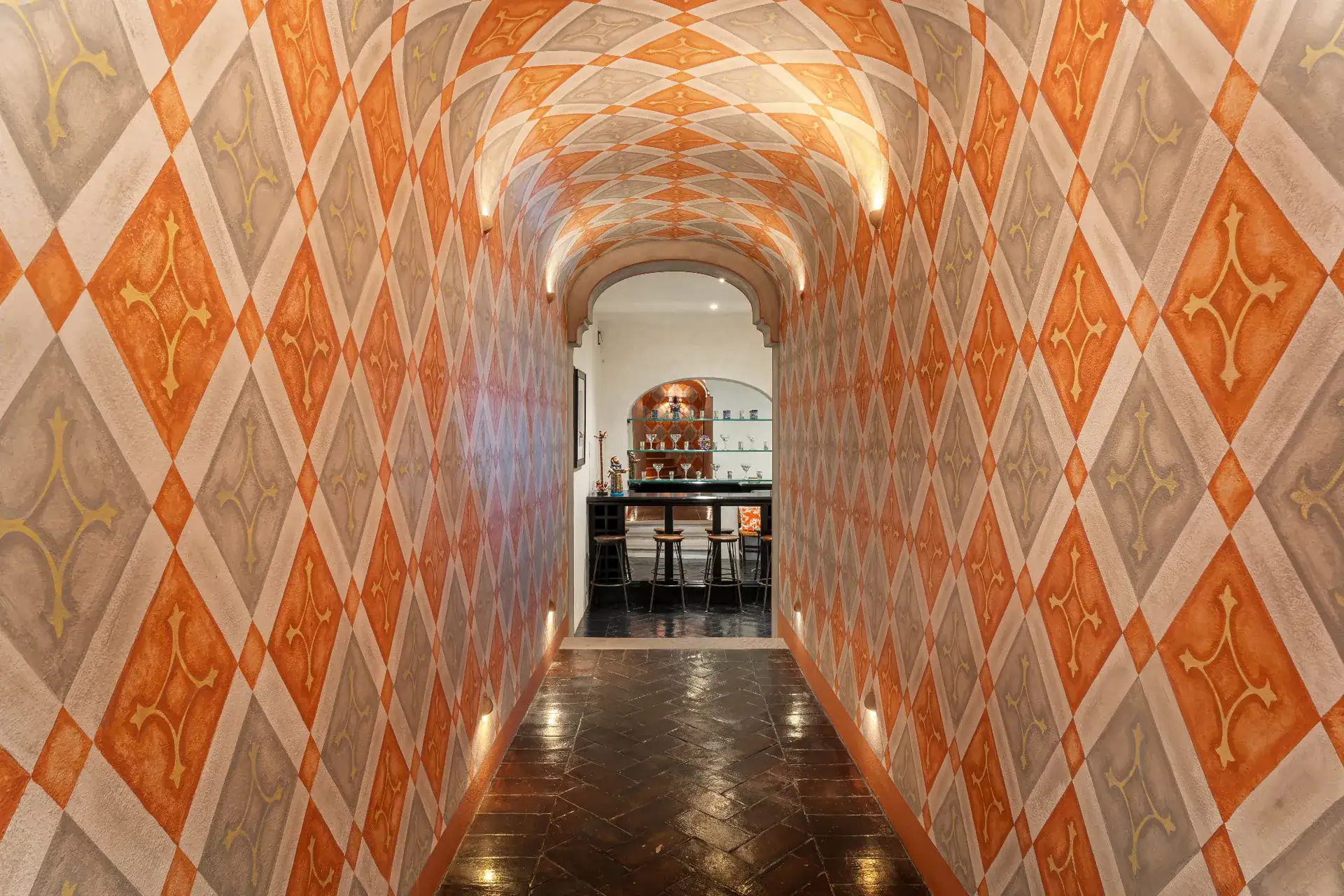 Casa Dos Casas, arched hallway with orange and gray diamond-patterned walls and a lit ceiling, San Miguel de Allende