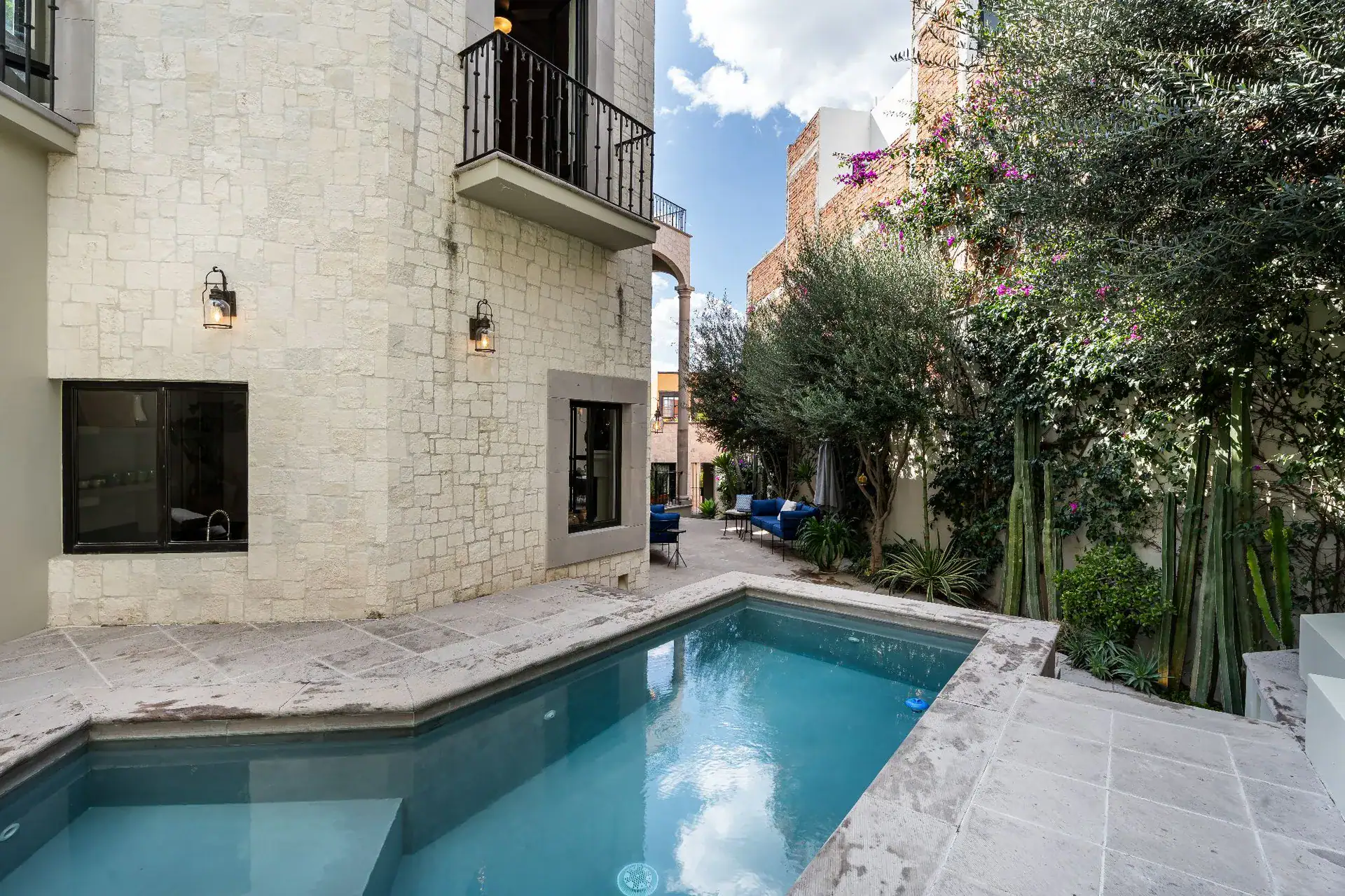 Casa Dos Casas, plunge pool beside a white stone wall with a balcony and garden trees, San Miguel de Allende