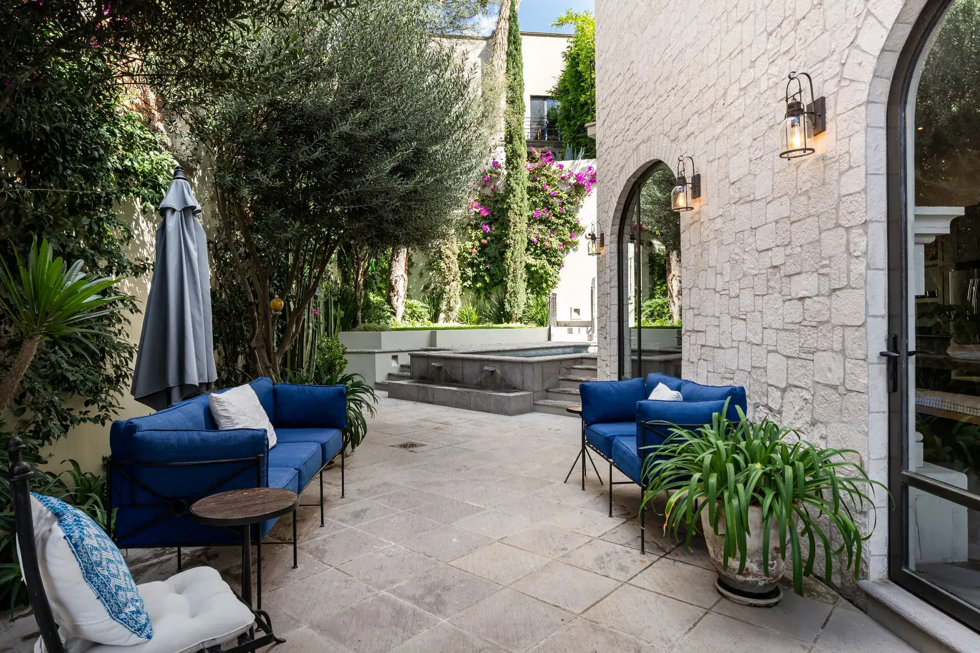 Casa Dos Casas, garden patio with blue outdoor seating, olive trees and an arched glass door, San Miguel de Allende