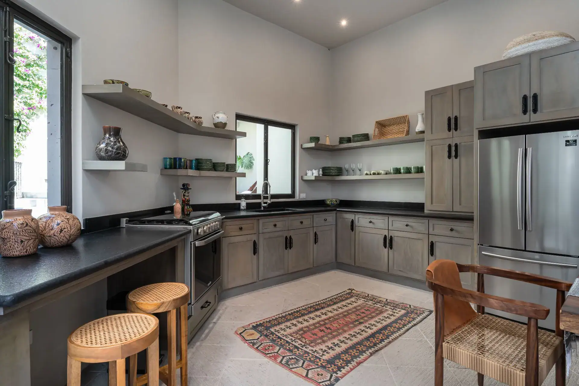 Casa Dos Casas, casita kitchen with gray cabinets, black counters, a stainless steel refrigerator and wooden stools, San Miguel de Allende
