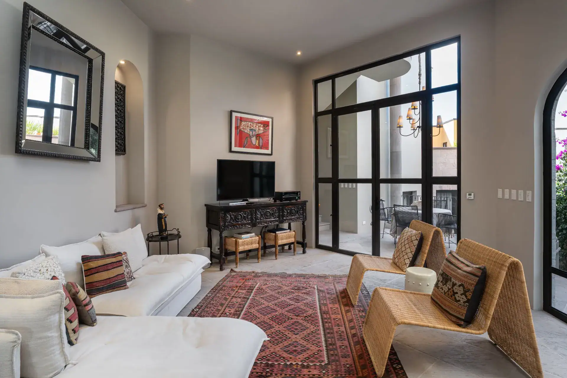 Casa Dos Casas, living room with a white sectional, woven chairs, red rug and black-framed glass doors, San Miguel de Allende