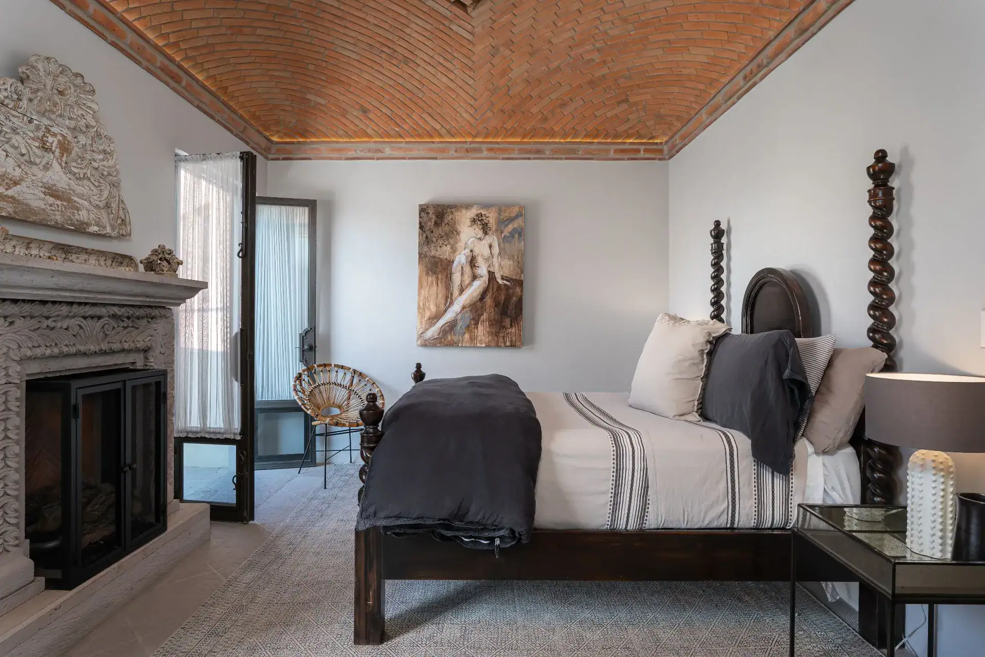 Casa Dos Casas, bedroom with a dark wood bed, stone fireplace and brick vaulted ceiling, San Miguel de Allende