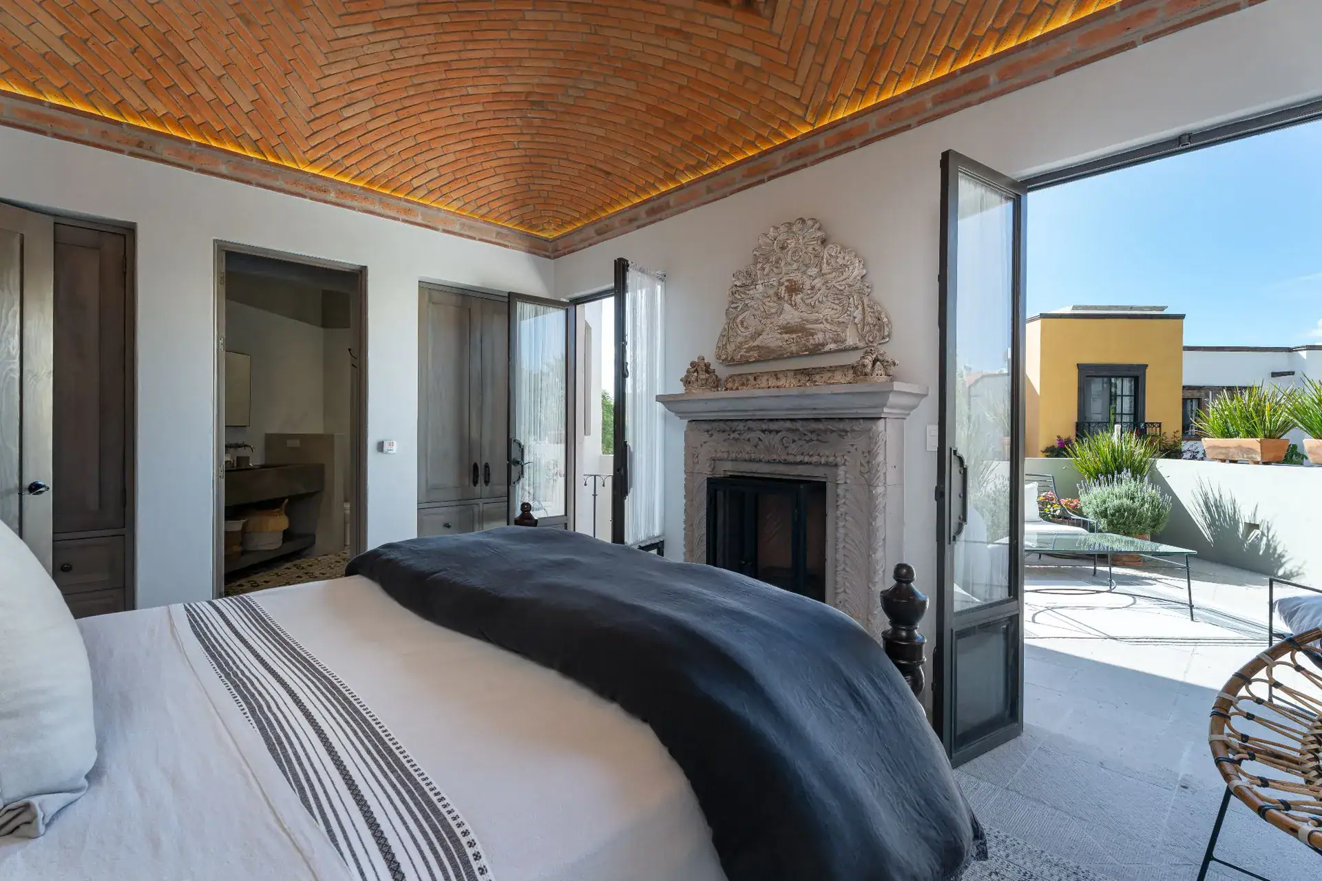 Casa Dos Casas, bedroom with a fireplace and a balcony door opening to a terrace under a brick vaulted ceiling, San Miguel de Allende