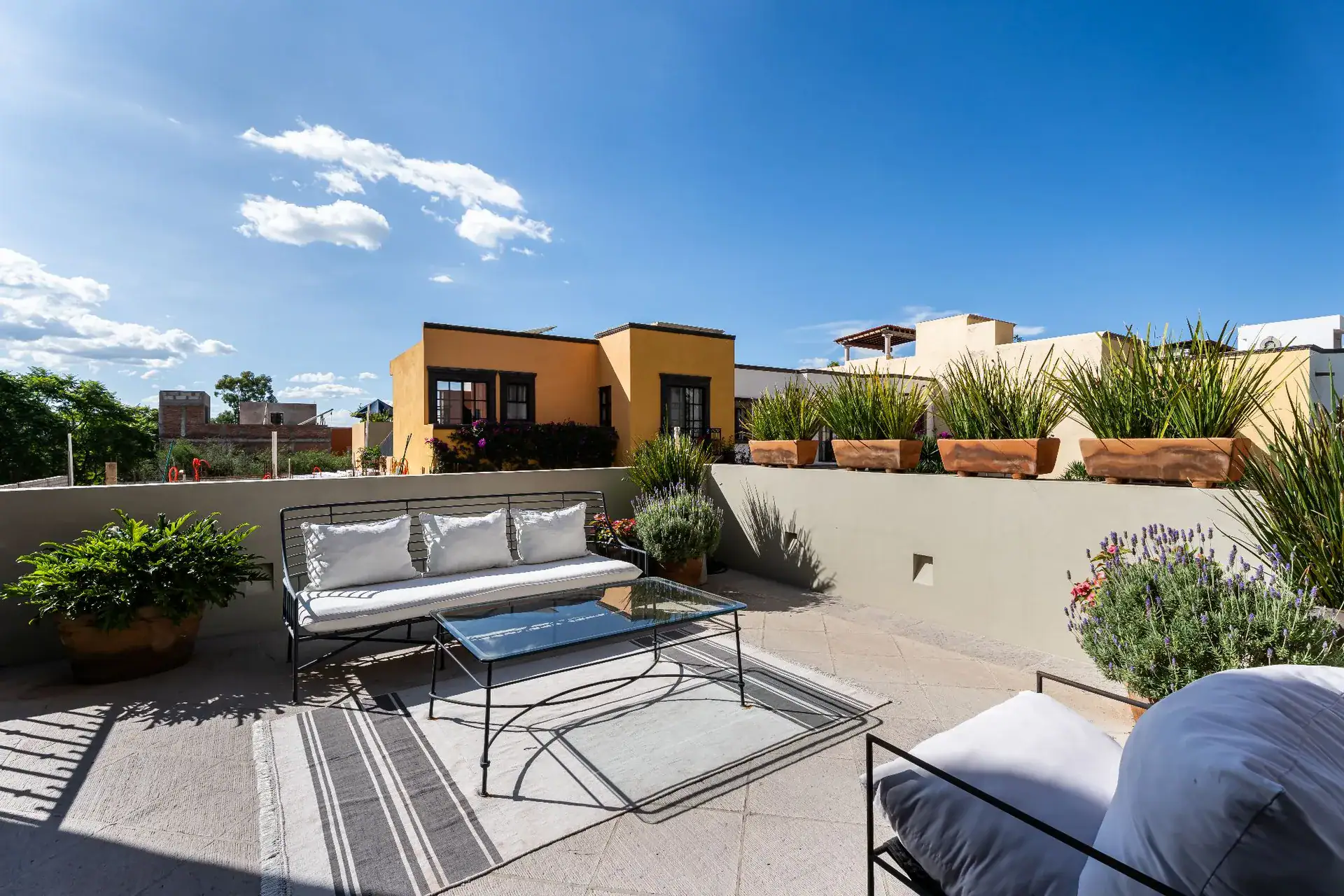Casa Dos Casas, rooftop terrace with white outdoor sofas, potted plants and a blue sky, San Miguel de Allende