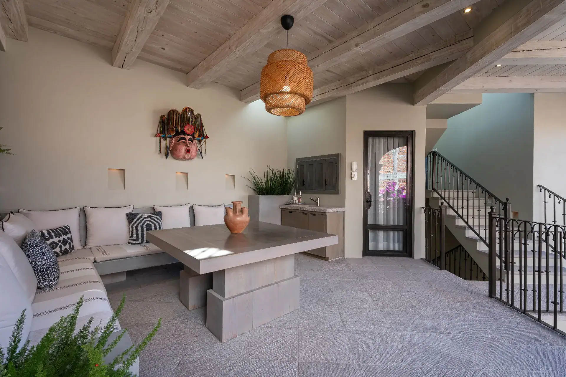 Casa Dos Casas, sitting room with a built-in sofa, concrete table, woven pendant light and a staircase, San Miguel de Allende