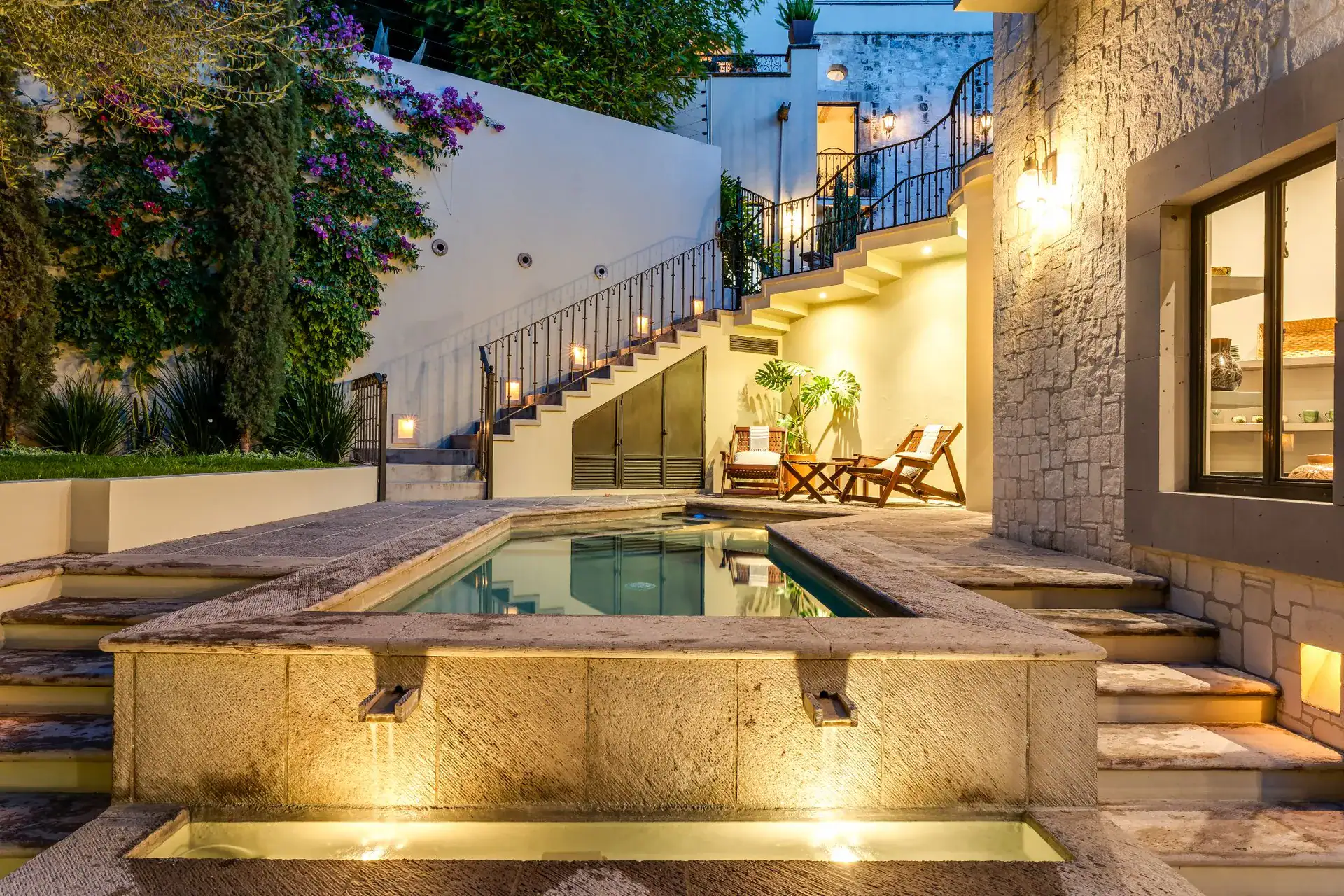 Casa Dos Casas, courtyard pool lit at dusk with a curved staircase and lounge chairs, San Miguel de Allende