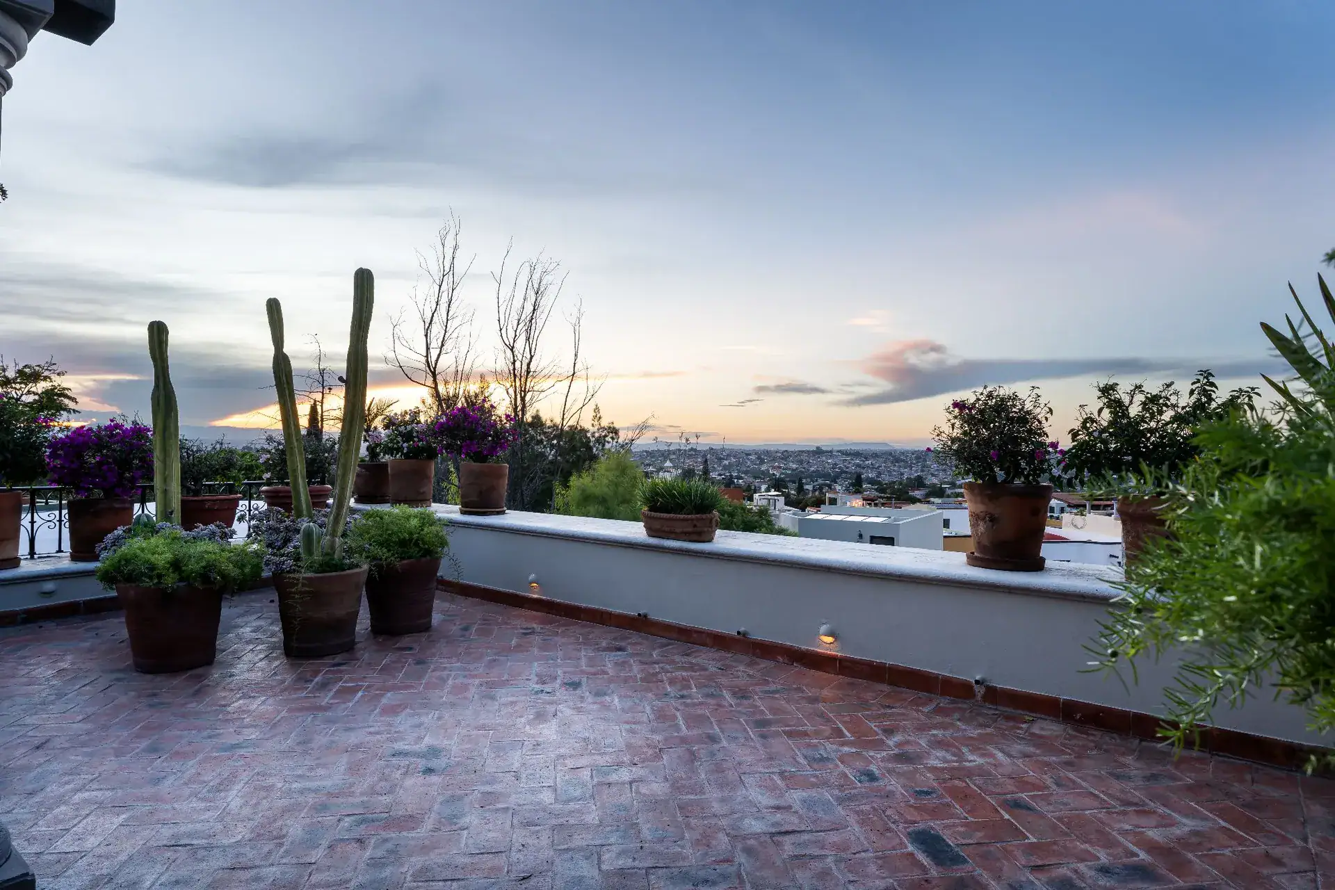 Casa Dos Casas, rooftop brick terrace with potted plants and cacti overlooking the town at sunset, San Miguel de Allende