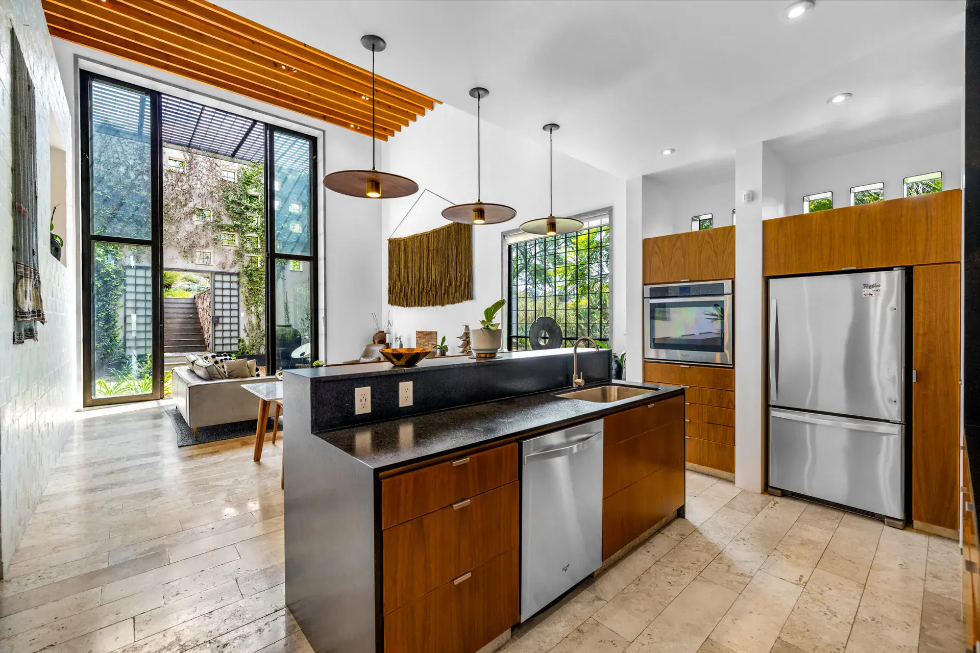 Casa Dos Gatos, kitchen with a black counter island, wood cabinets, a stainless refrigerator and tall steel-framed windows to a courtyard, San Miguel de Allende