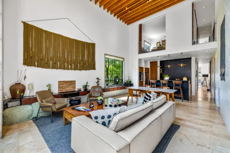 Casa Dos Gatos, double-height living room with a cream sofa, leather armchairs, a woven wall hanging and a wood-slat ceiling, San Miguel de Allende