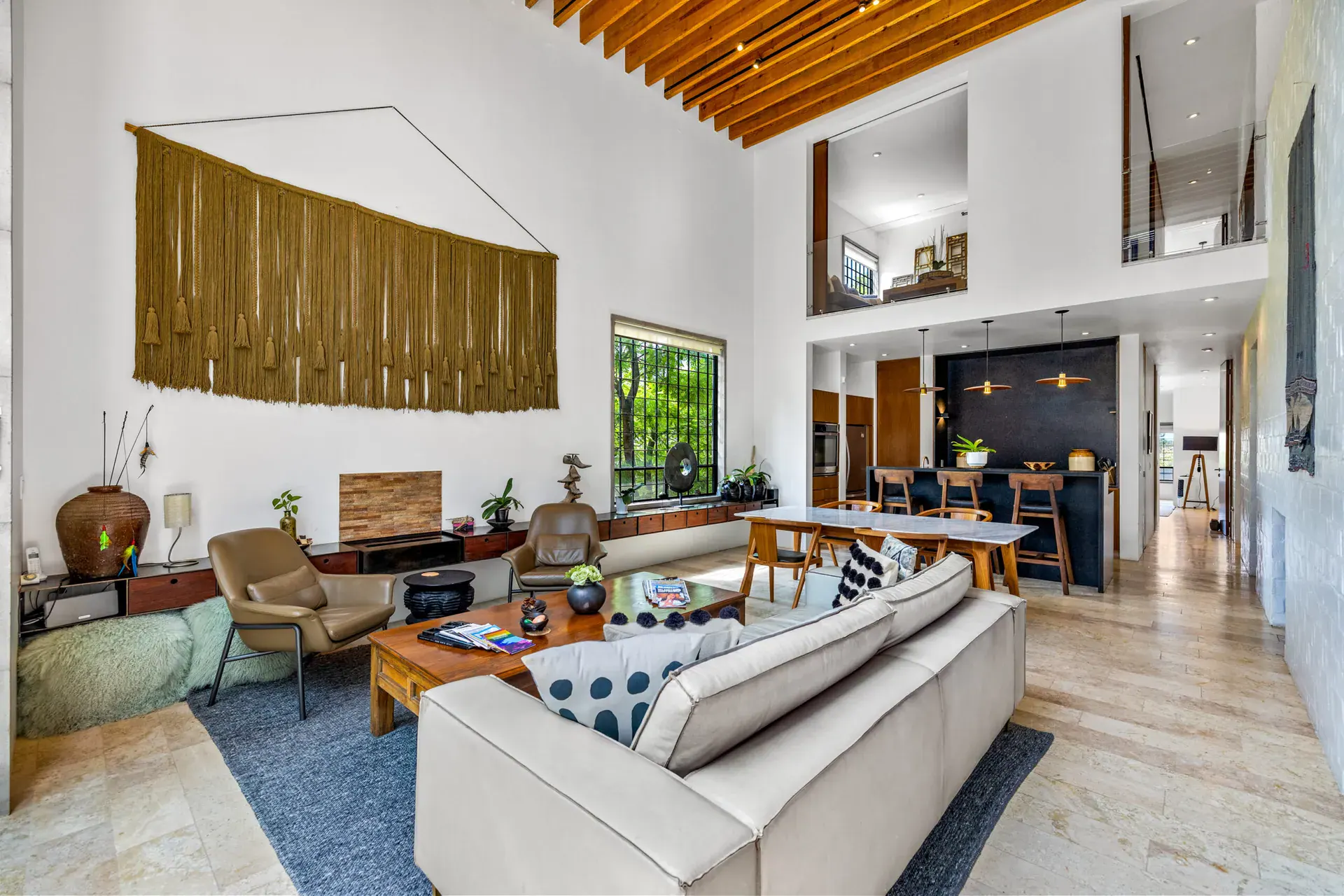 Casa Dos Gatos, double-height living room with a cream sofa, leather armchairs, a woven wall hanging and a wood-slat ceiling, San Miguel de Allende