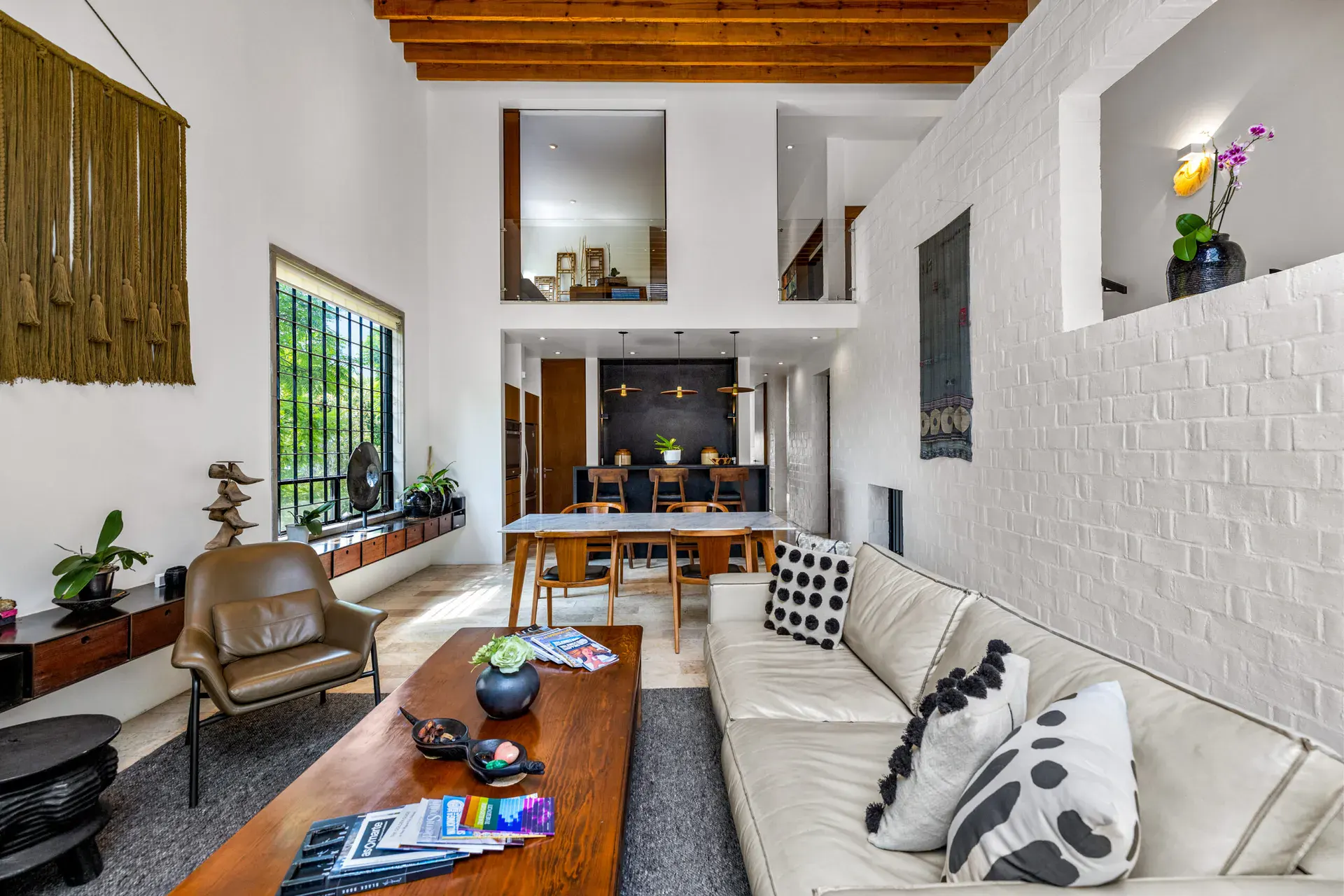 Casa Dos Gatos, living room with a long sofa, a wood coffee table and a mezzanine above the dining area, San Miguel de Allende