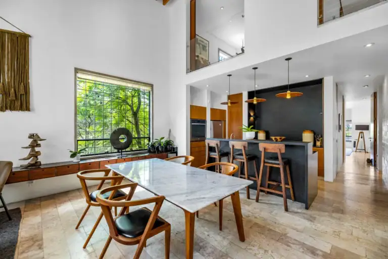 Casa Dos Gatos, dining table with a marble top, wood chairs, an island with stools and a green window view, San Miguel de Allende