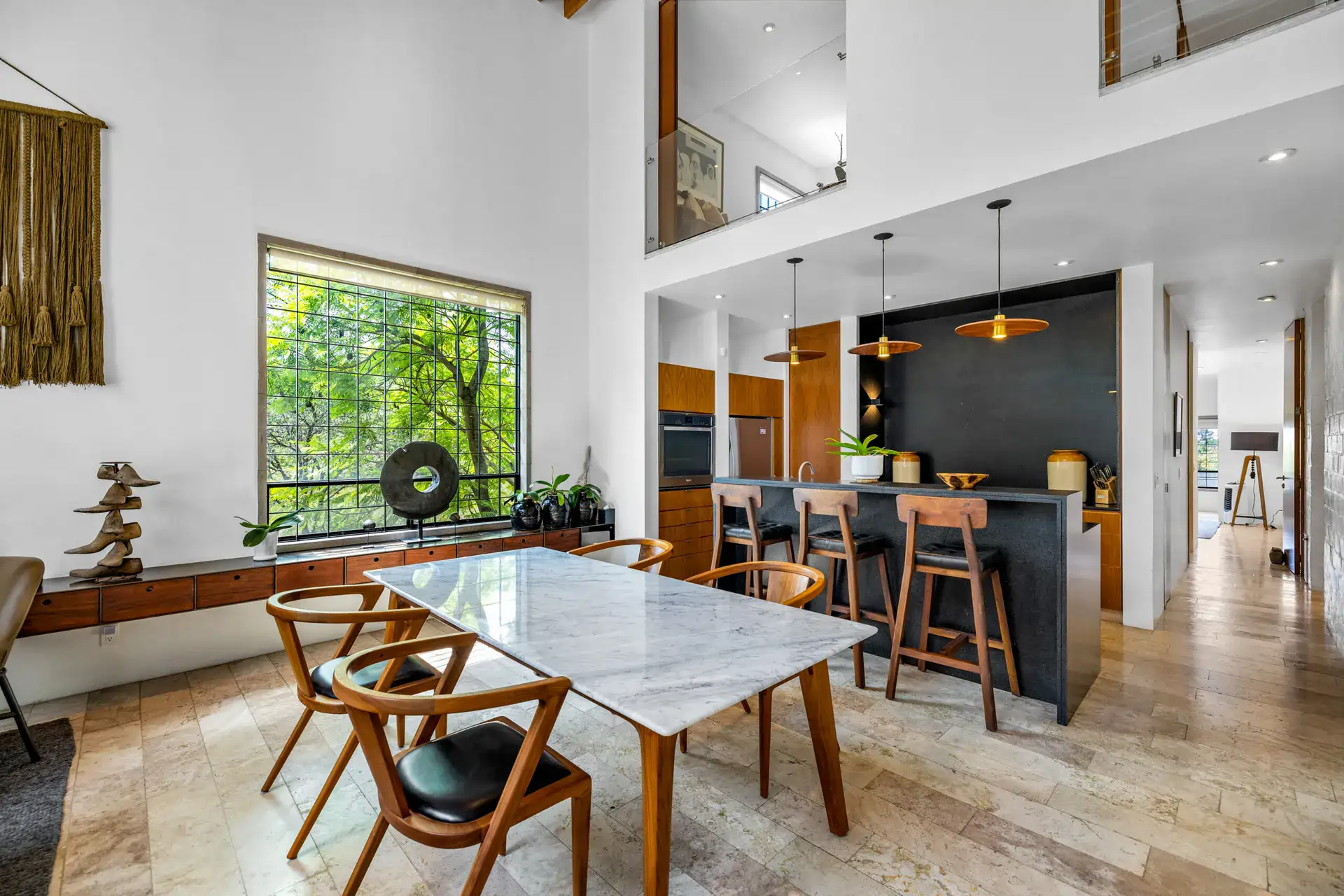 Casa Dos Gatos, dining table with a marble top, wood chairs, an island with stools and a green window view, San Miguel de Allende