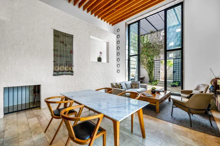 Casa Dos Gatos, dining area and living room with a steel-framed glass wall to a planted courtyard, San Miguel de Allende