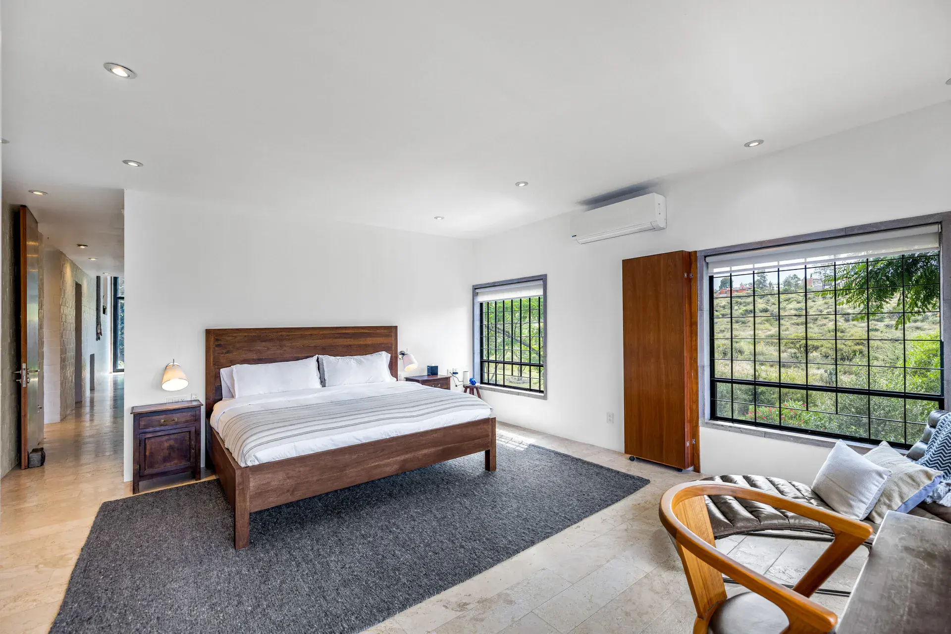 Casa Dos Gatos, bedroom with a wood bed, a gray rug and a large window with a view of the hills, San Miguel de Allende