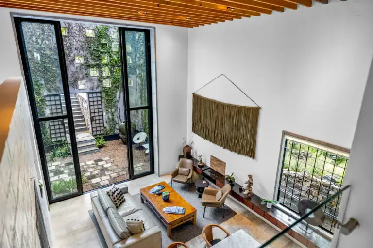 Casa Dos Gatos, view from the mezzanine down to the living room and the courtyard through a tall glass wall, San Miguel de Allende