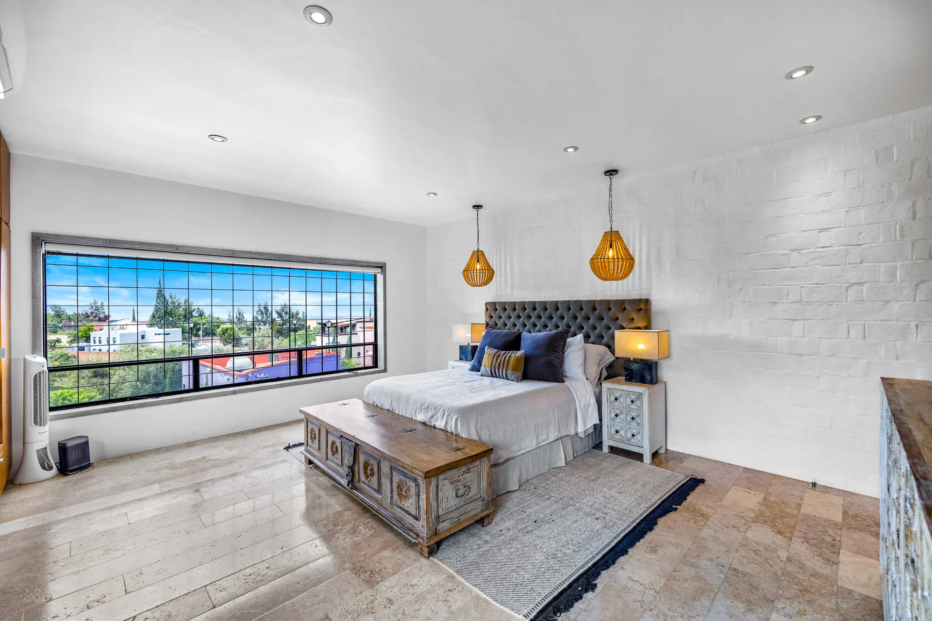 Casa Dos Gatos, bedroom with a tufted headboard, a carved wood chest and a long window over the neighborhood, San Miguel de Allende
