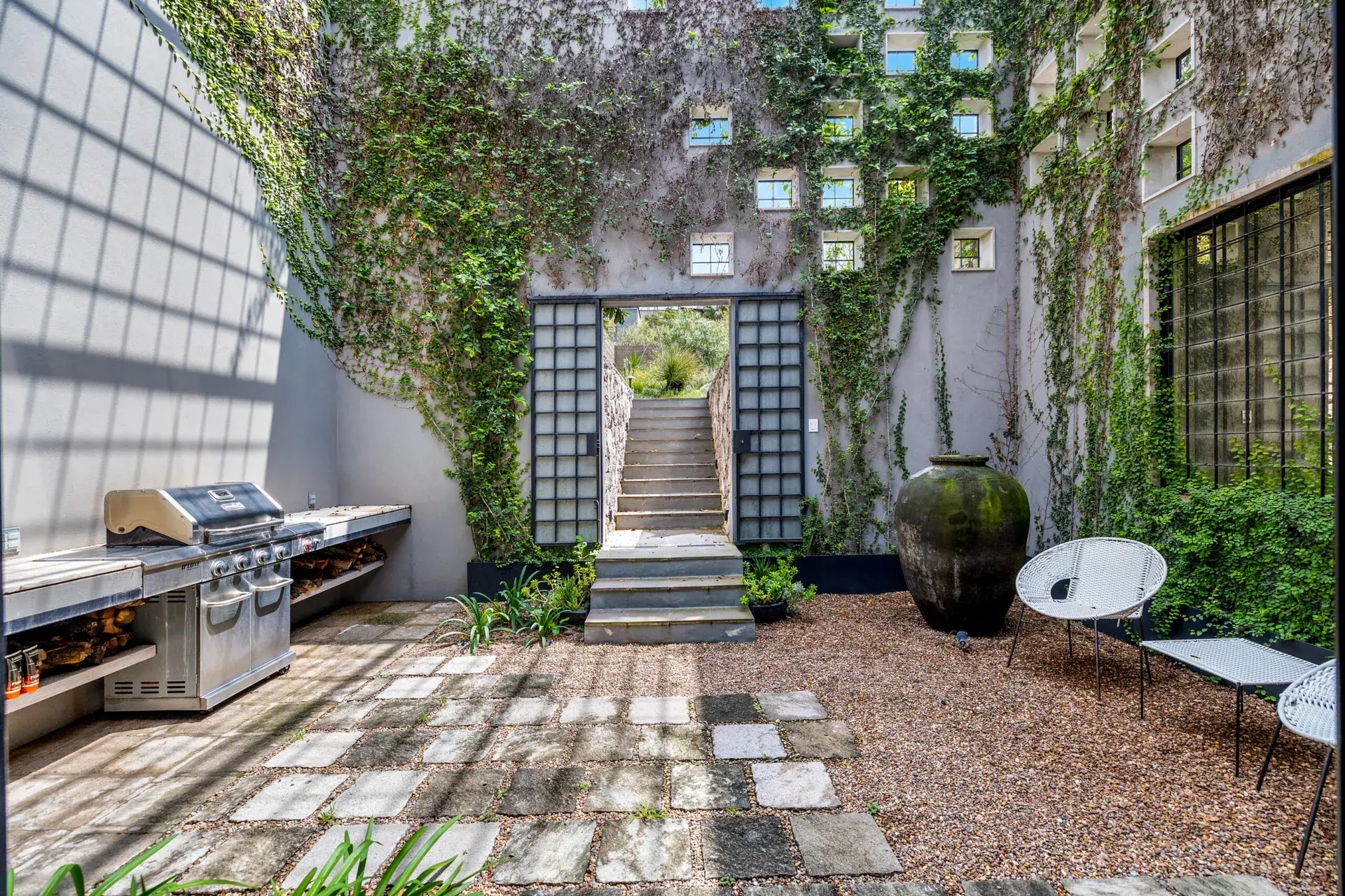 Casa Dos Gatos, courtyard with a barbecue, a stone staircase, a large clay urn and vines on a gray wall, San Miguel de Allende