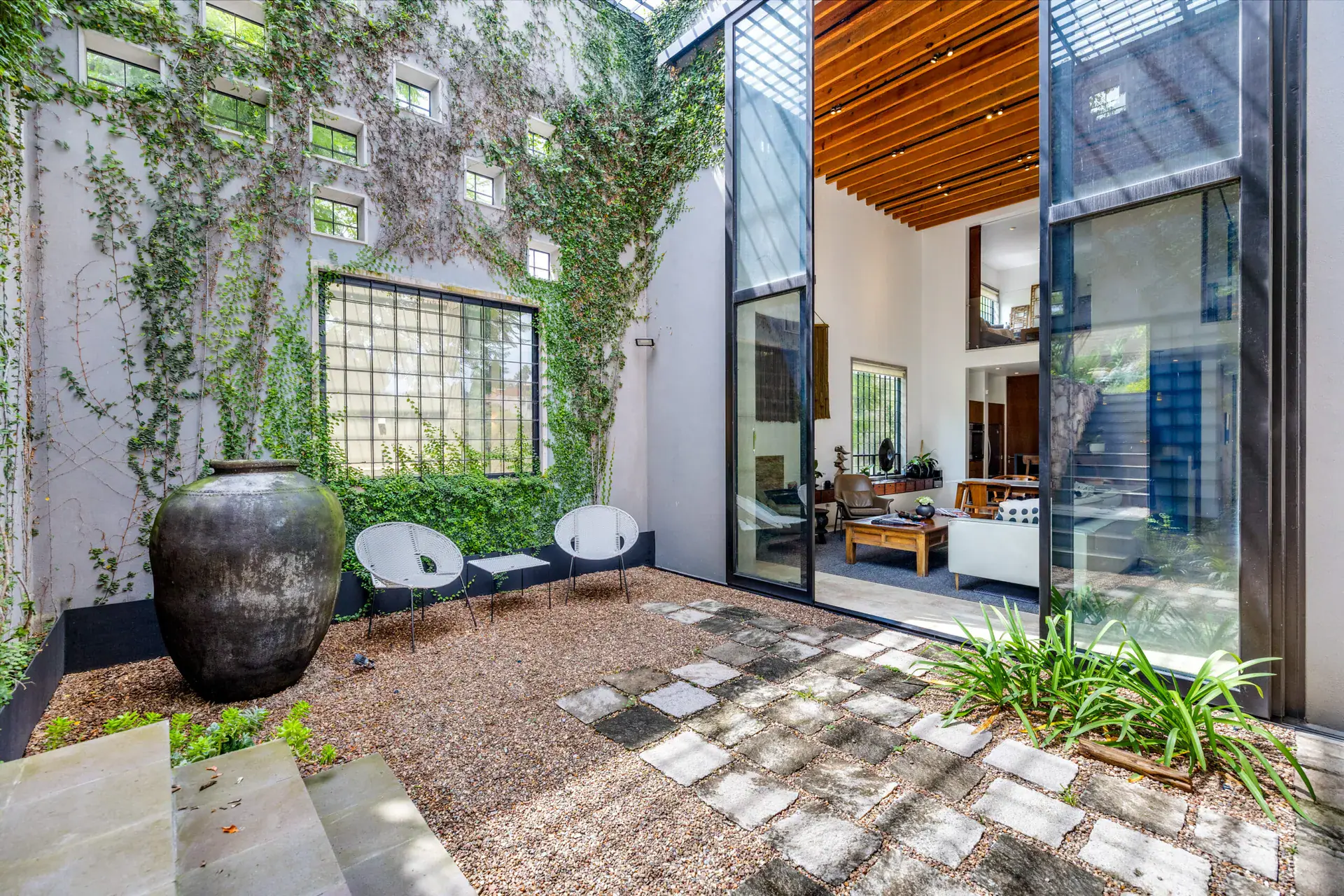 Casa Dos Gatos, courtyard with a large clay urn, white chairs, stone pavers and glass doors into the house, San Miguel de Allende