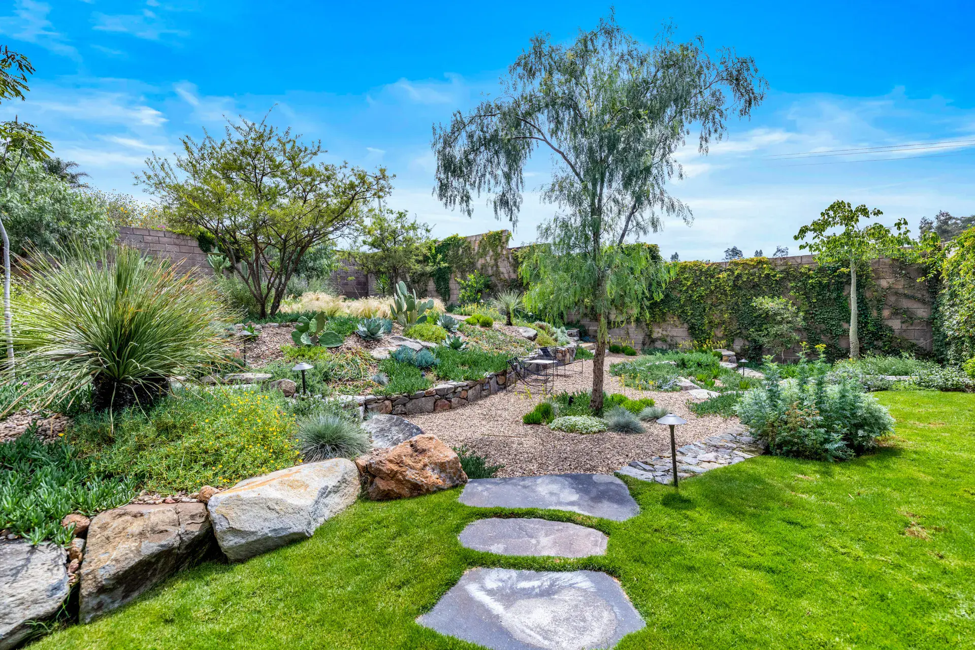 Casa Dos Gatos, garden with a lawn, flagstone steps, boulders and a tree in a landscaped yard, San Miguel de Allende