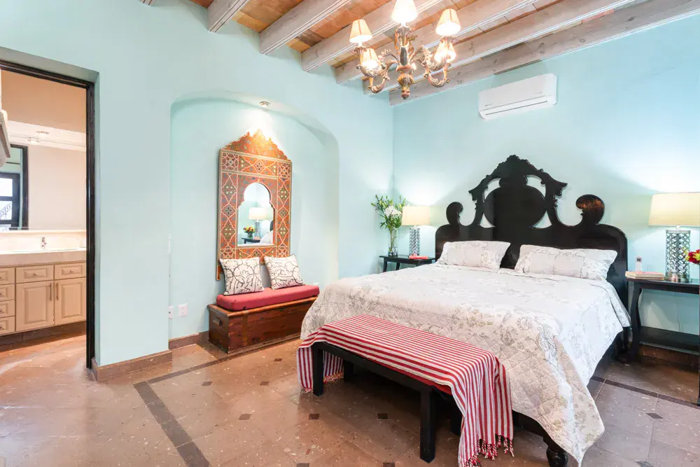 Casa Elegante, primary bedroom with a carved dark headboard and a turquoise wall, San Miguel de Allende