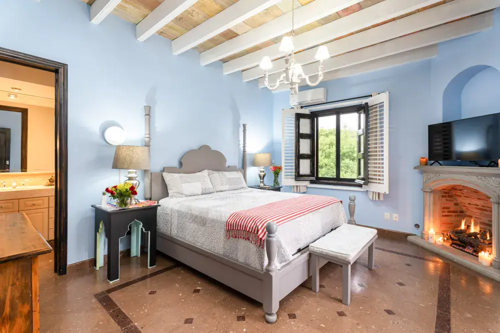 Casa Elegante, bedroom with a blue wall, a corner fireplace and a window to the street, San Miguel de Allende