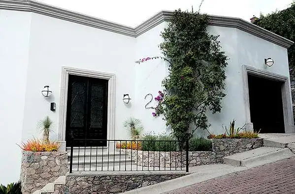 Casa Eloísa, street entrance with a black iron door and a garage beside a stone wall, San Miguel de Allende
