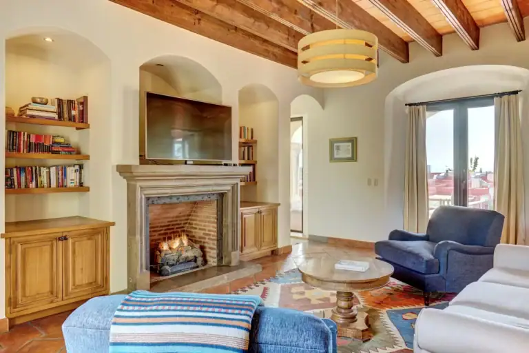Casa Familia, family room with a stone fireplace, built-in shelves and a blue armchair, San Miguel de Allende