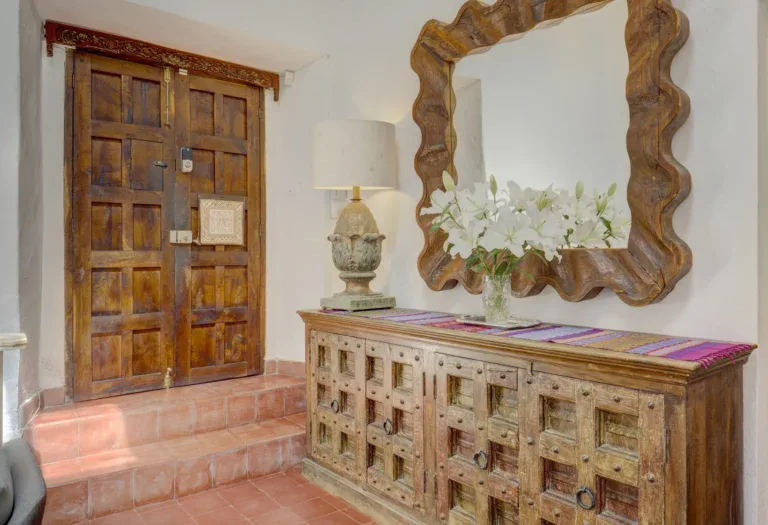 Casa Firenze, entry with a carved double wooden door, a carved sideboard with a lamp and a wavy wood-framed mirror, San Miguel de Allende