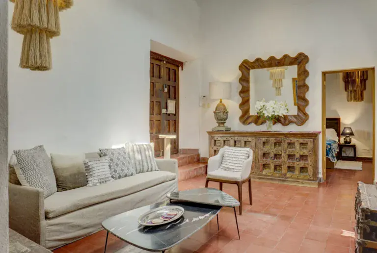 Casa Firenze, living room with a linen sofa, a carved sideboard and mirror, a white armchair and a stone-top coffee table, San Miguel de Allende