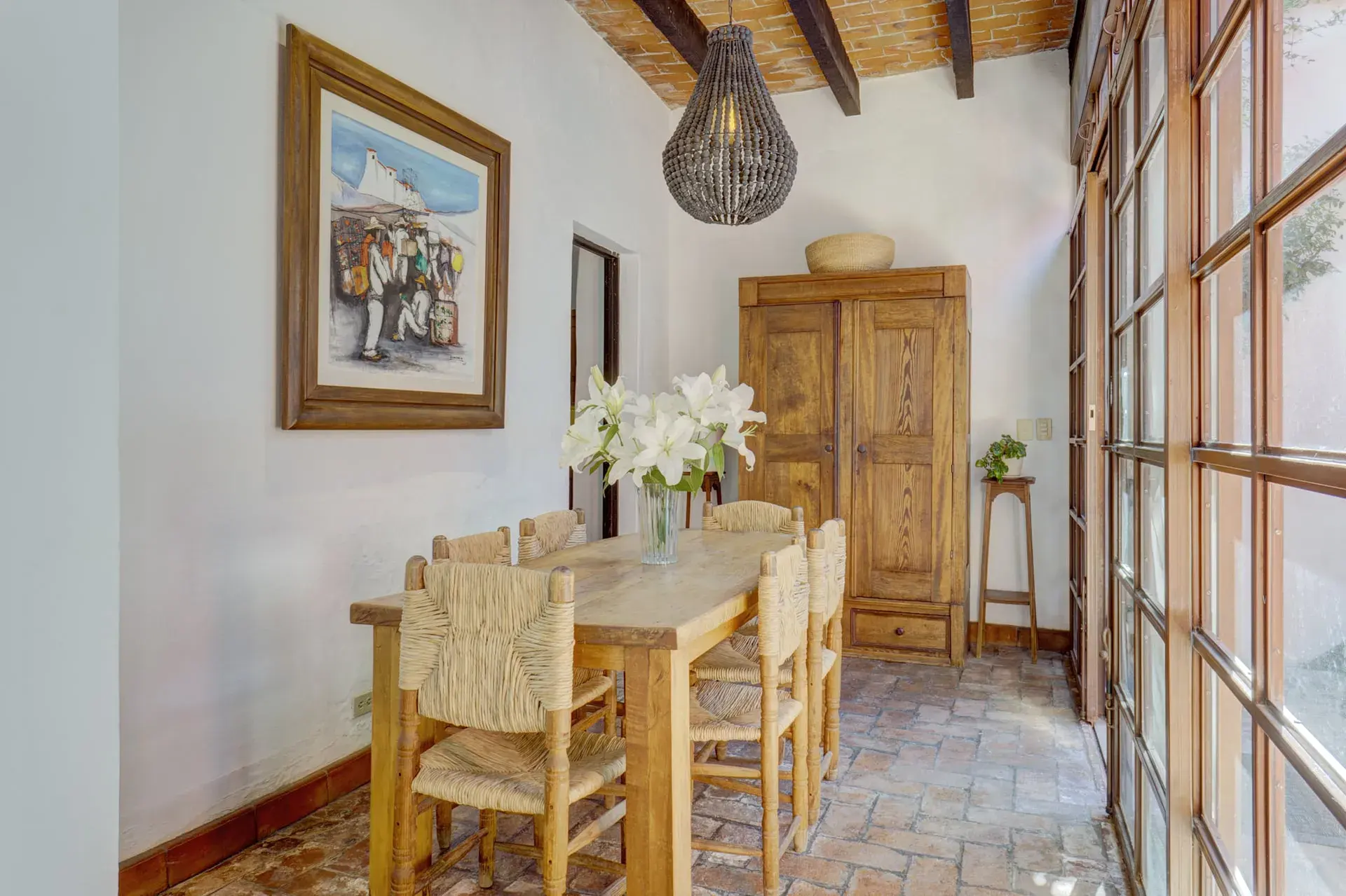 Casa Firenze, dining table with woven chairs, a wood armoire, a framed painting and a steel-framed glass wall, San Miguel de Allende