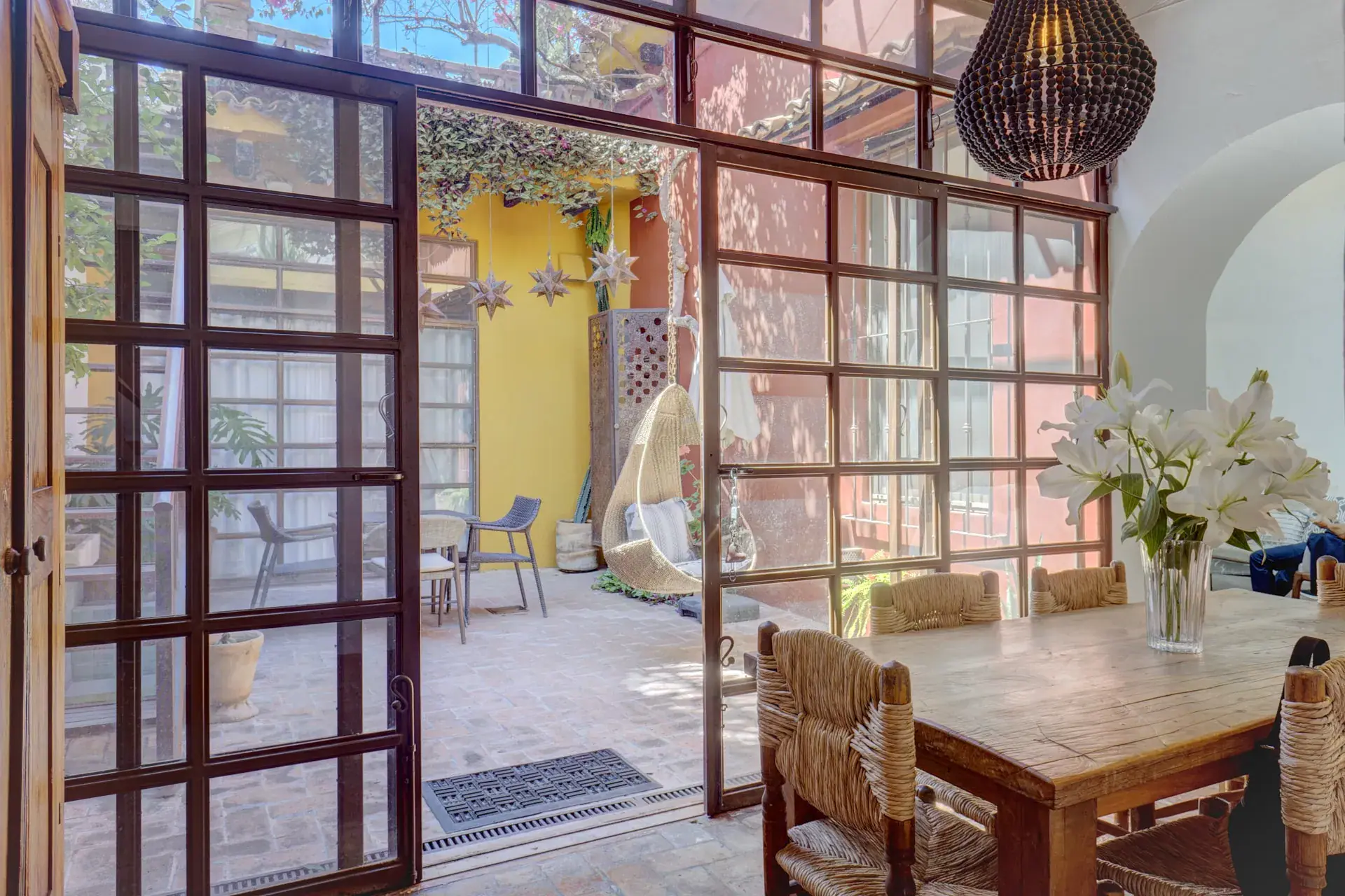 Casa Firenze, dining table beside a steel-framed glass wall opening to a courtyard with a hanging chair, San Miguel de Allende
