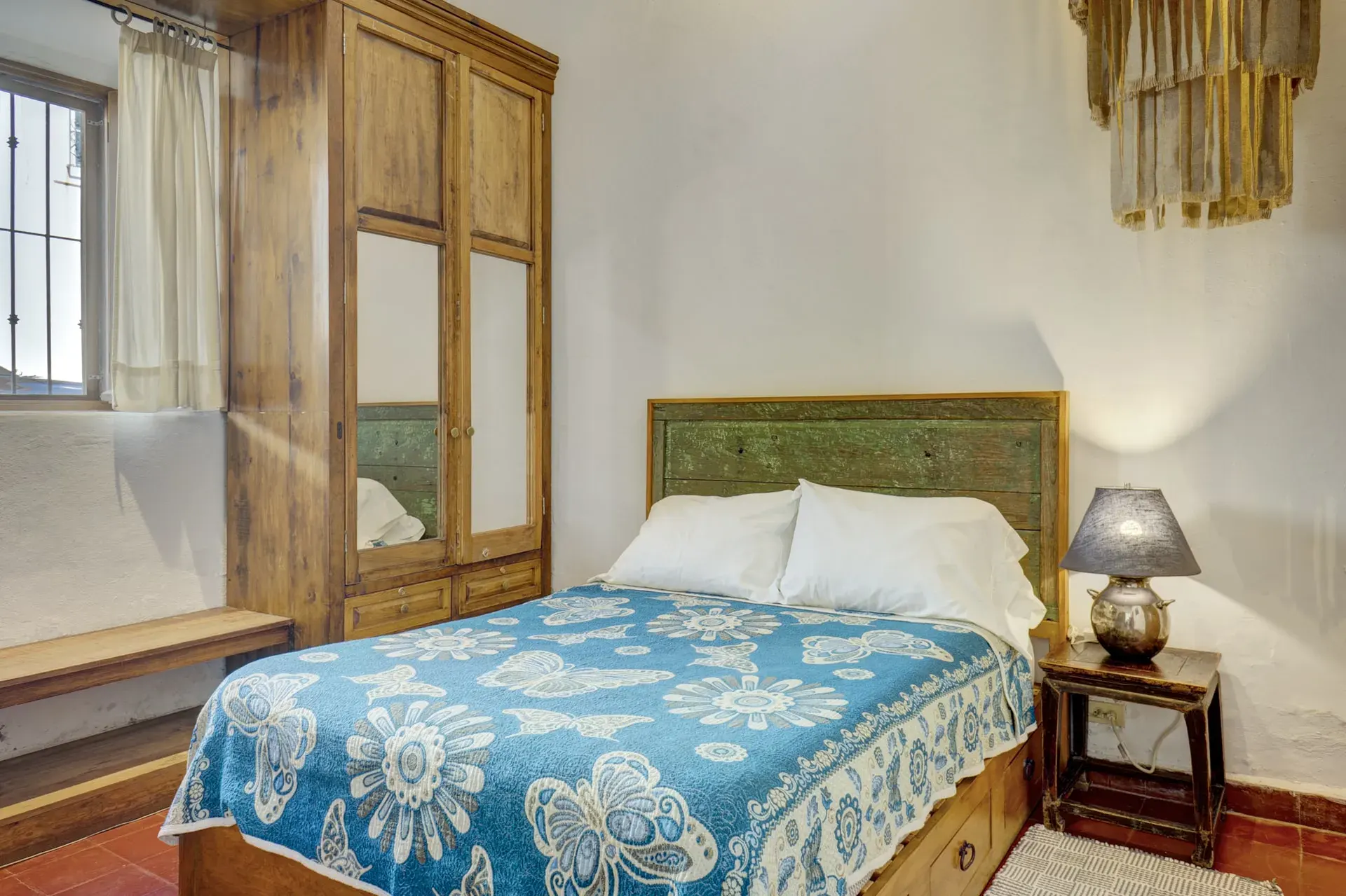 Casa Firenze, bedroom with a green headboard, a blue floral bedspread, a wood armoire and a window seat, San Miguel de Allende