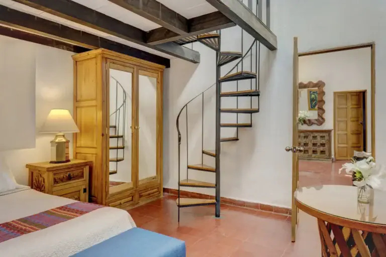 Casa Firenze, bedroom with a carved nightstand, a mirrored armoire and a spiral staircase to a loft, San Miguel de Allende
