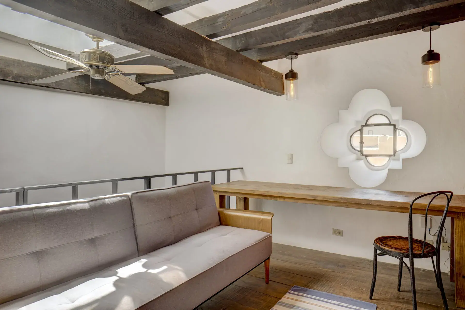Casa Firenze, loft den with a gray sofa, a desk, a ceiling fan and a quatrefoil window, San Miguel de Allende