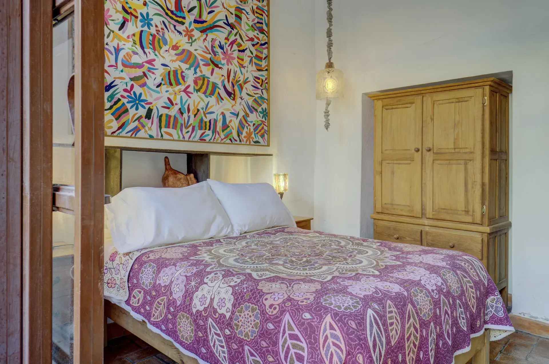 Casa Firenze, bedroom with a purple bedspread, a colorful embroidered wall hanging and a wood armoire, San Miguel de Allende