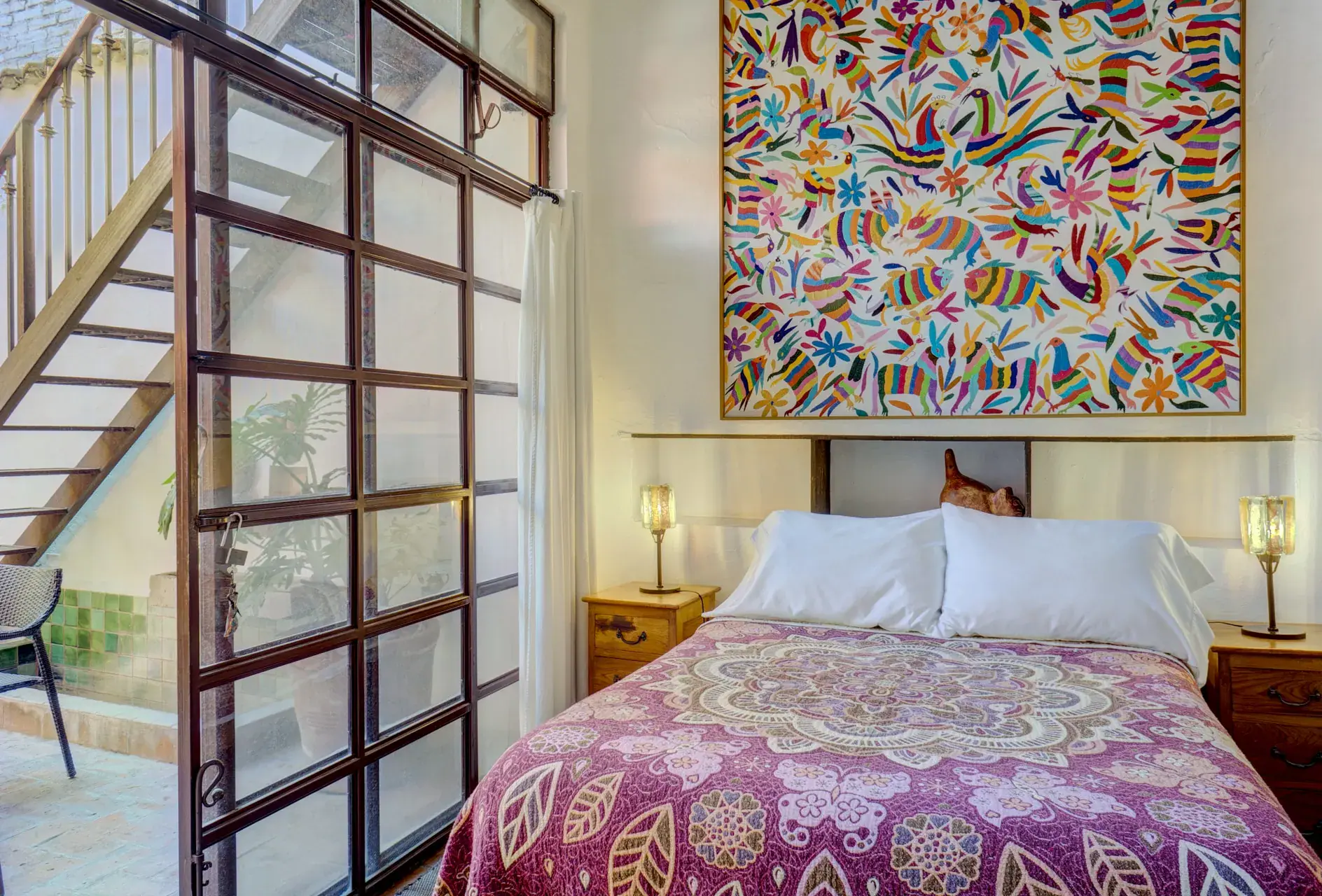 Casa Firenze, bedroom with a purple bedspread, an embroidered textile and a steel-framed glass wall to the courtyard, San Miguel de Allende