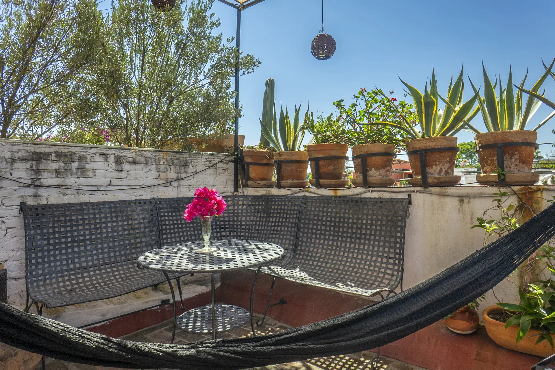 Casa Firenze, rooftop terrace with a metal corner sofa, a round table, potted agaves and a hammock, San Miguel de Allende