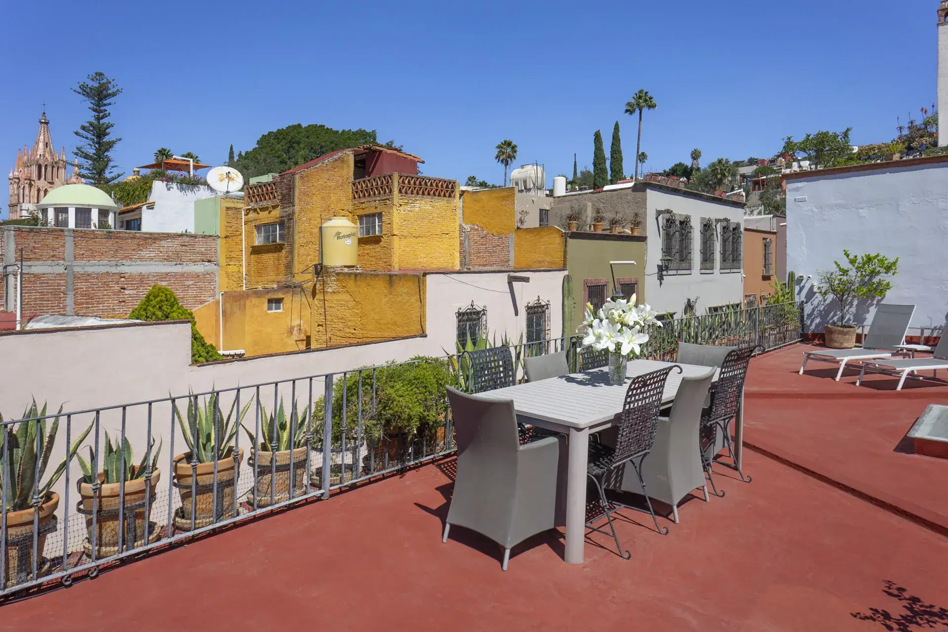 Casa Firenze, rooftop terrace with a dining table and chairs, potted agaves and a view of town and the Parroquia, San Miguel de Allende