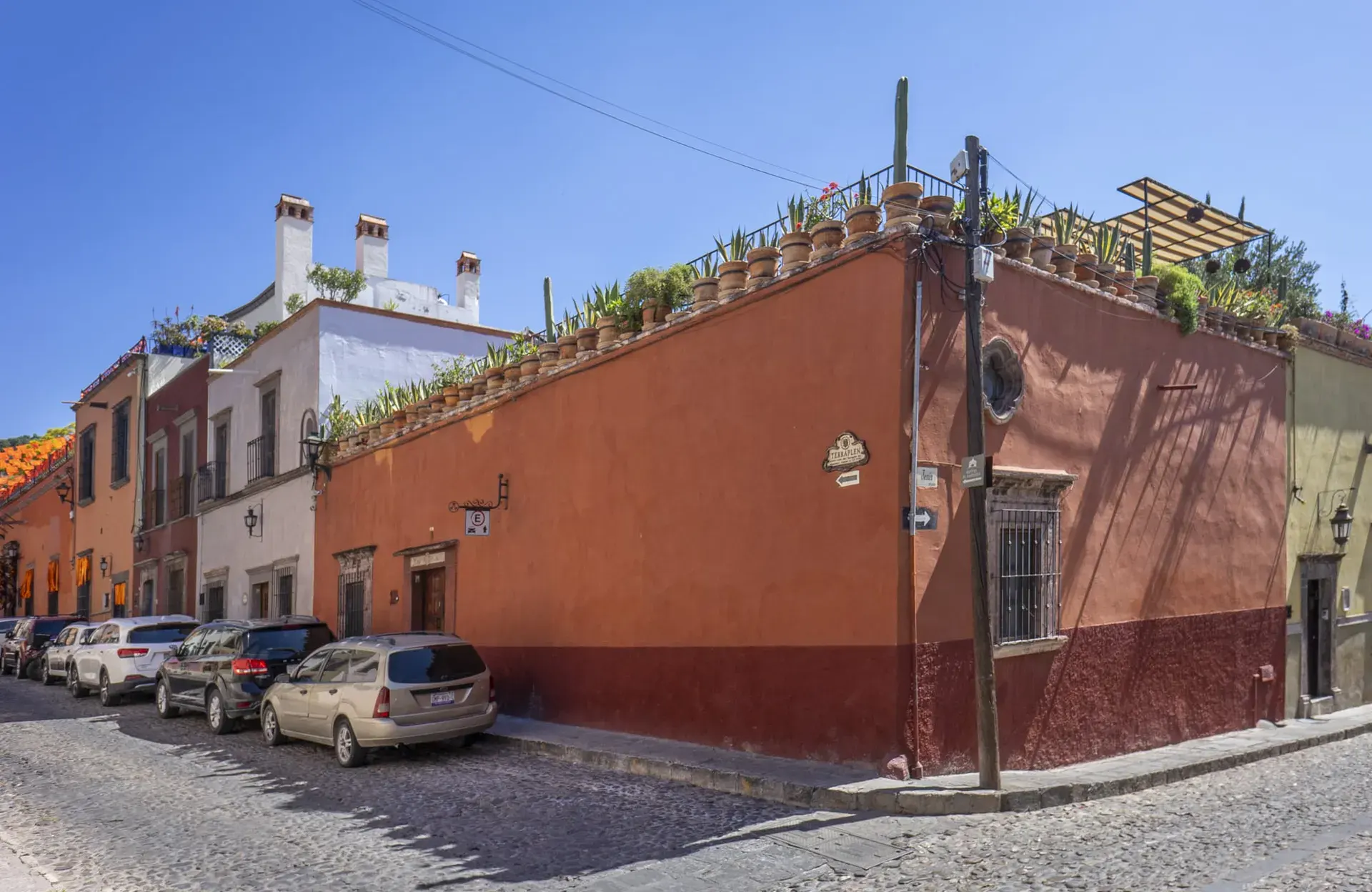 Casa Firenze, red-ochre corner facade of the house on a cobblestone street with a rooftop garden, San Miguel de Allende