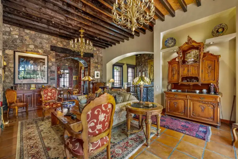 Casa Flora, living room with ornate armchairs, a carved wood hutch and a view into the next room, San Miguel de Allende