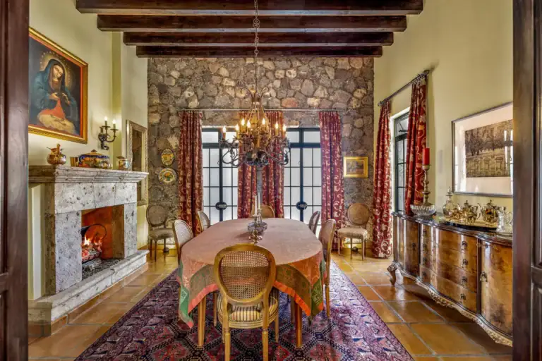Casa Flora, dining room with an oval table, a stone fireplace, a stone wall and red drapes, San Miguel de Allende