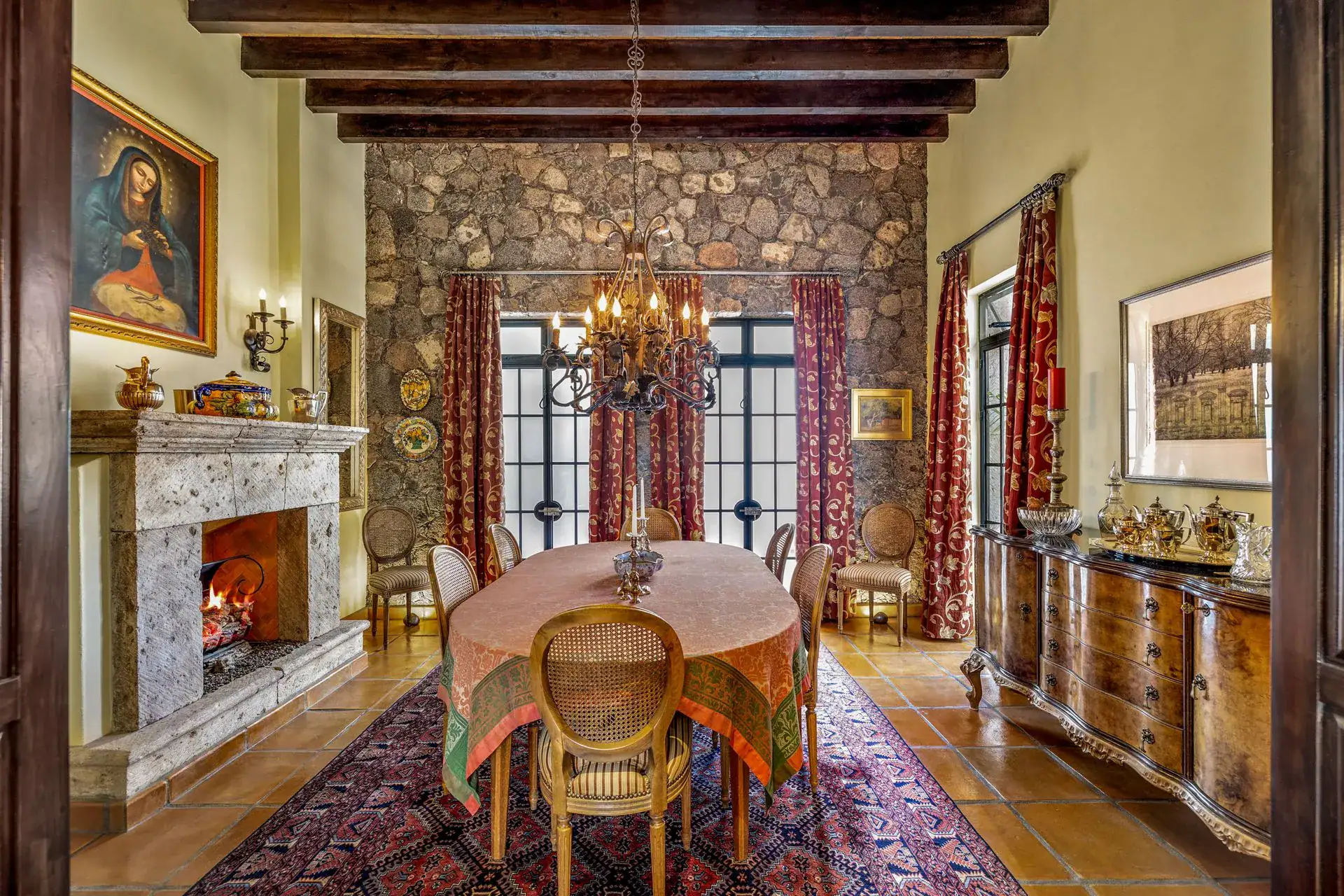 Casa Flora, dining room with an oval table, a stone fireplace, a stone wall and red drapes, San Miguel de Allende