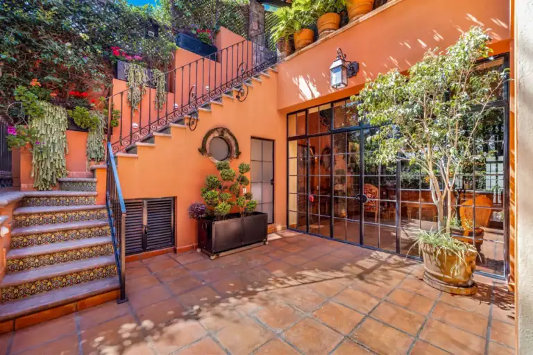 Casa Flora, courtyard with a tiled staircase, an orange wall and a steel-framed glass door, San Miguel de Allende