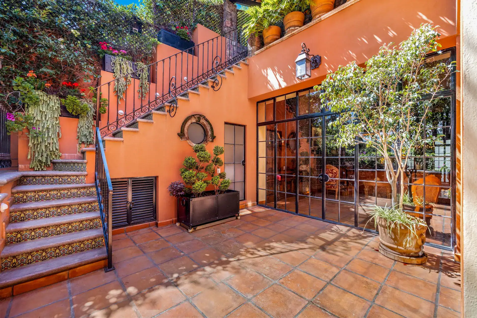 Casa Flora, courtyard with a tiled staircase, an orange wall and a steel-framed glass door, San Miguel de Allende