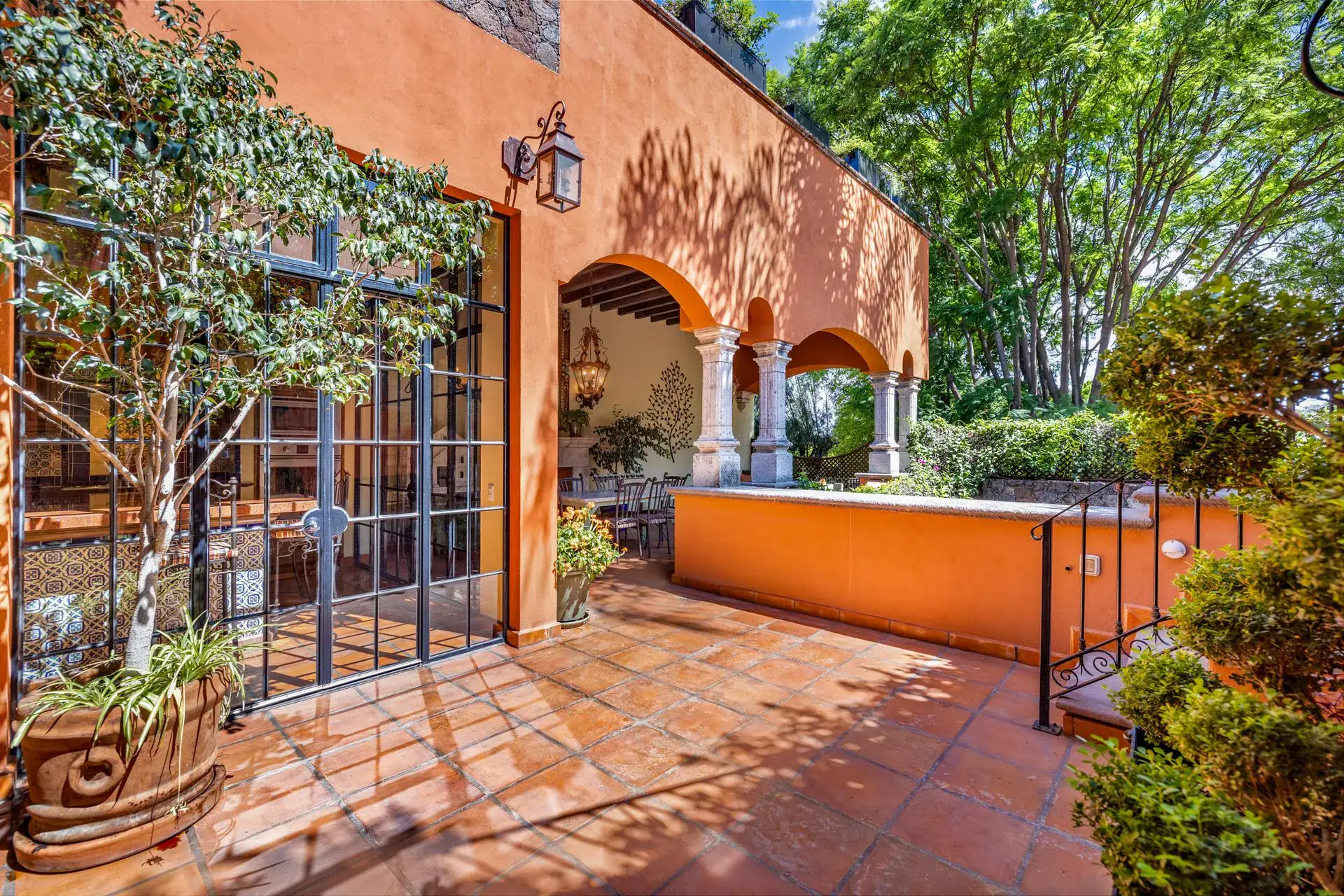 Casa Flora, courtyard terrace with orange walls, an arched loggia and tall trees, San Miguel de Allende