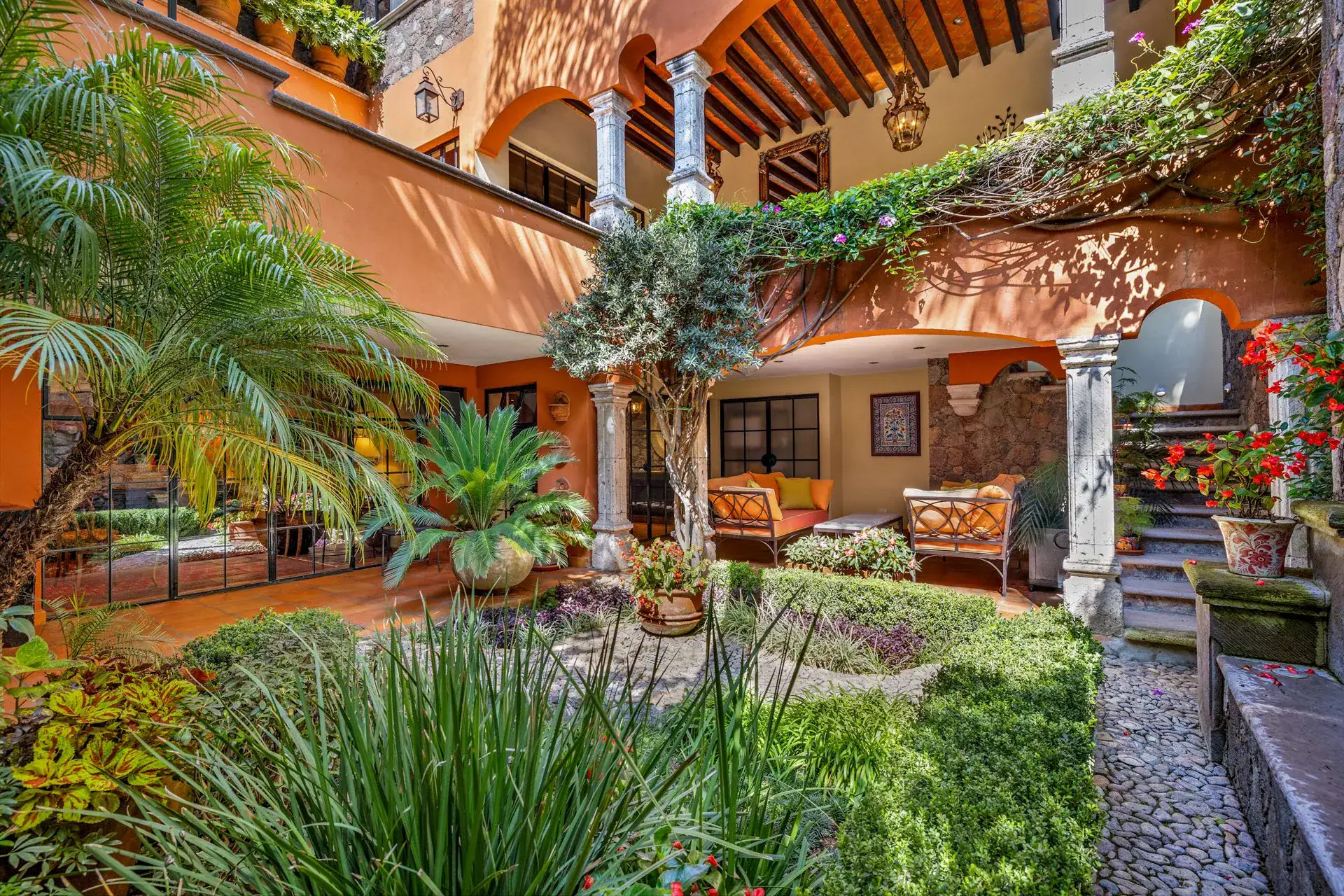 Casa Flora, garden courtyard with palms, a pebble path and a covered loggia with seating, San Miguel de Allende